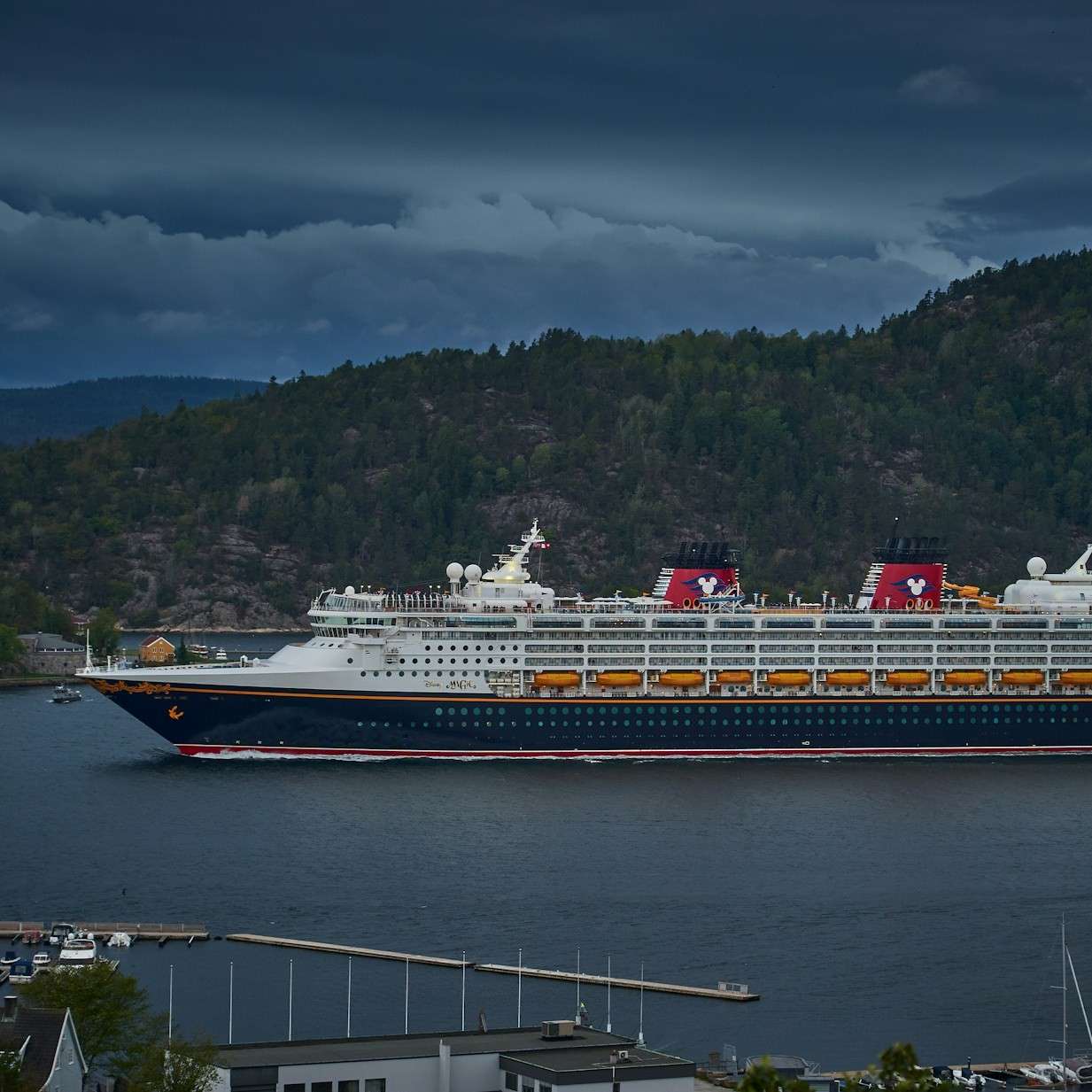 large blue, white, and yellow ocean cruise ship in a cold Alaskan bay with mountain trees in background