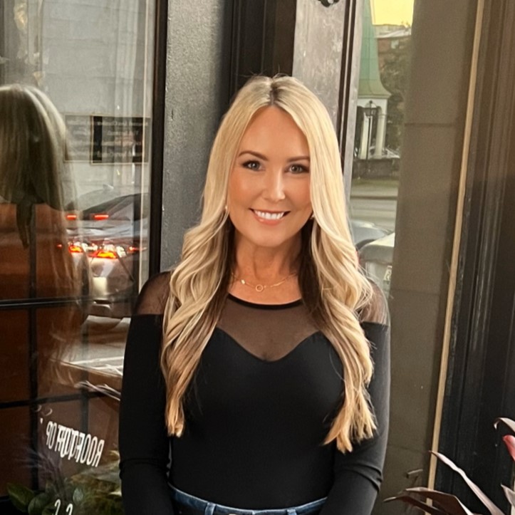 smiling blonde woman with tight black shirt sleeves and hair curled back in layered wings