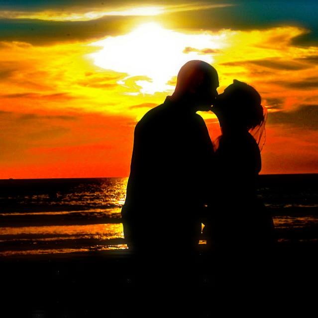 kissing couple silhouetted on beach at sunset